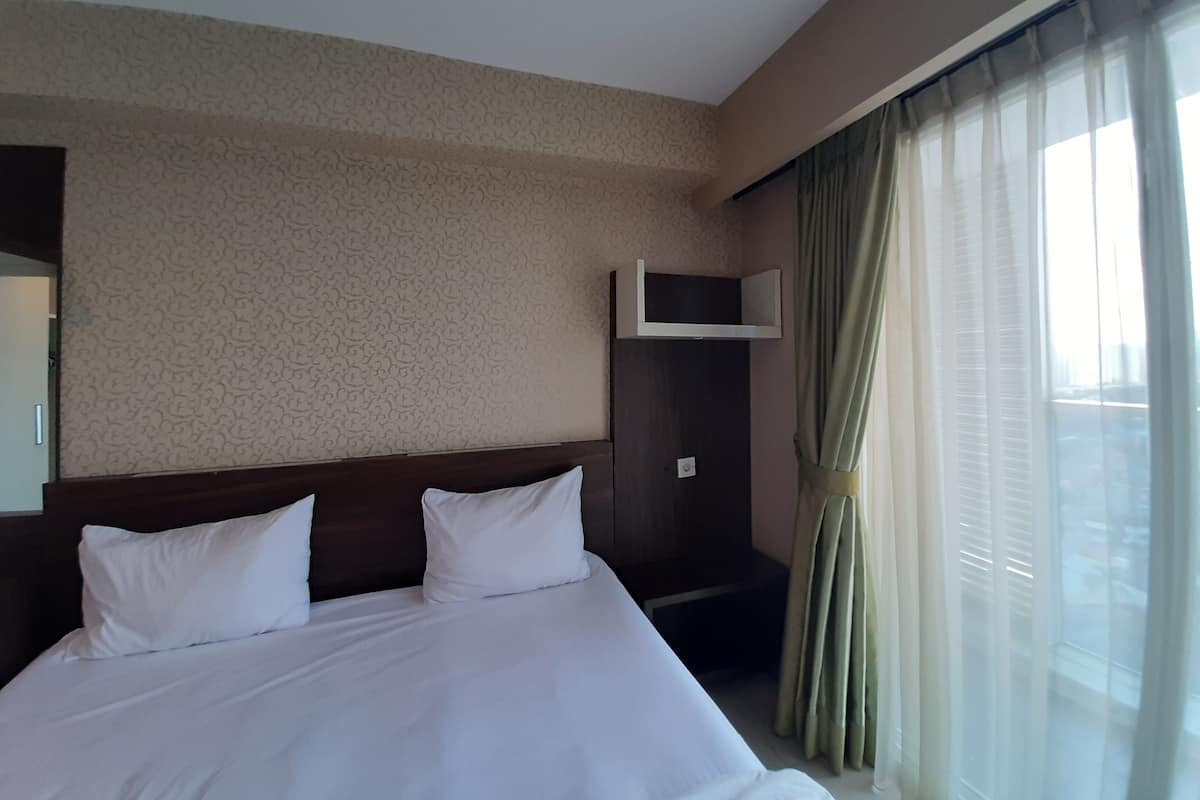 Habitación de hotel con una cama grande, un cabecero, un televisor instalado en la pared y una ventana con cortinas.