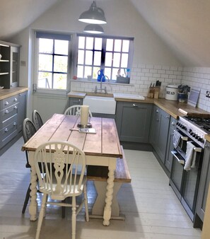 Uma cozinha com mesa e cadeiras de madeira, pia, fogão e janela com vista para árvores.