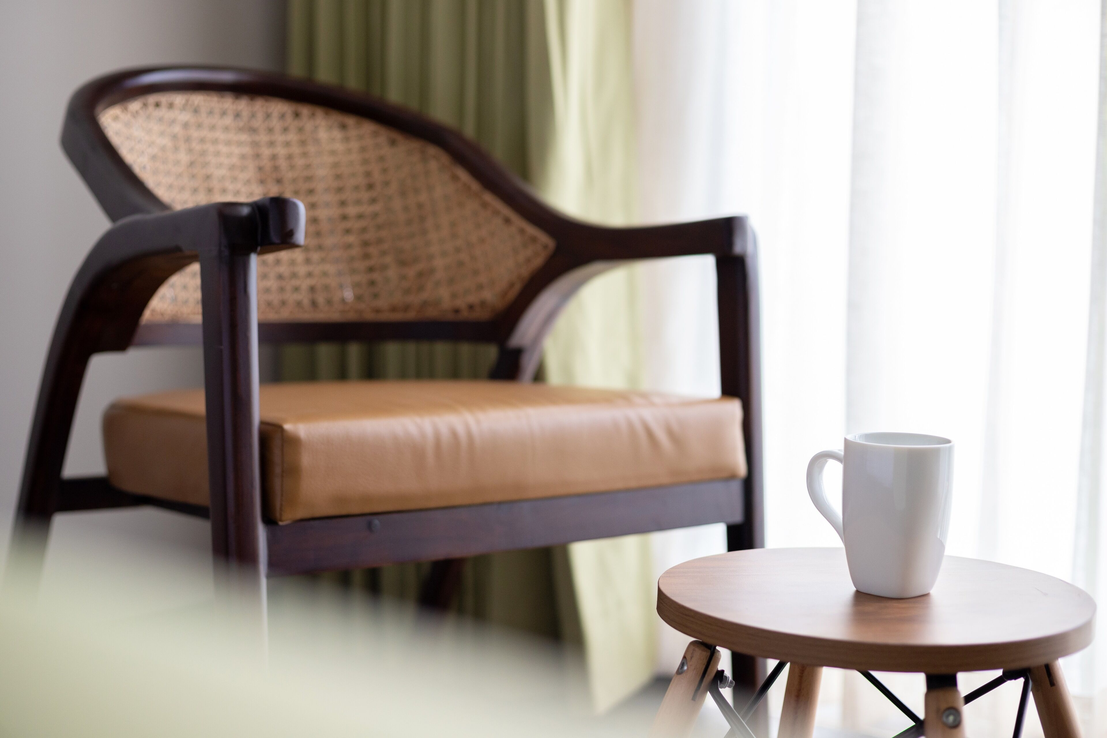Une chaise en bois avec un dossier en osier et un siège en cuir, placée à côté d’une petite table ronde en bois sur laquelle se trouve une tasse blanche.