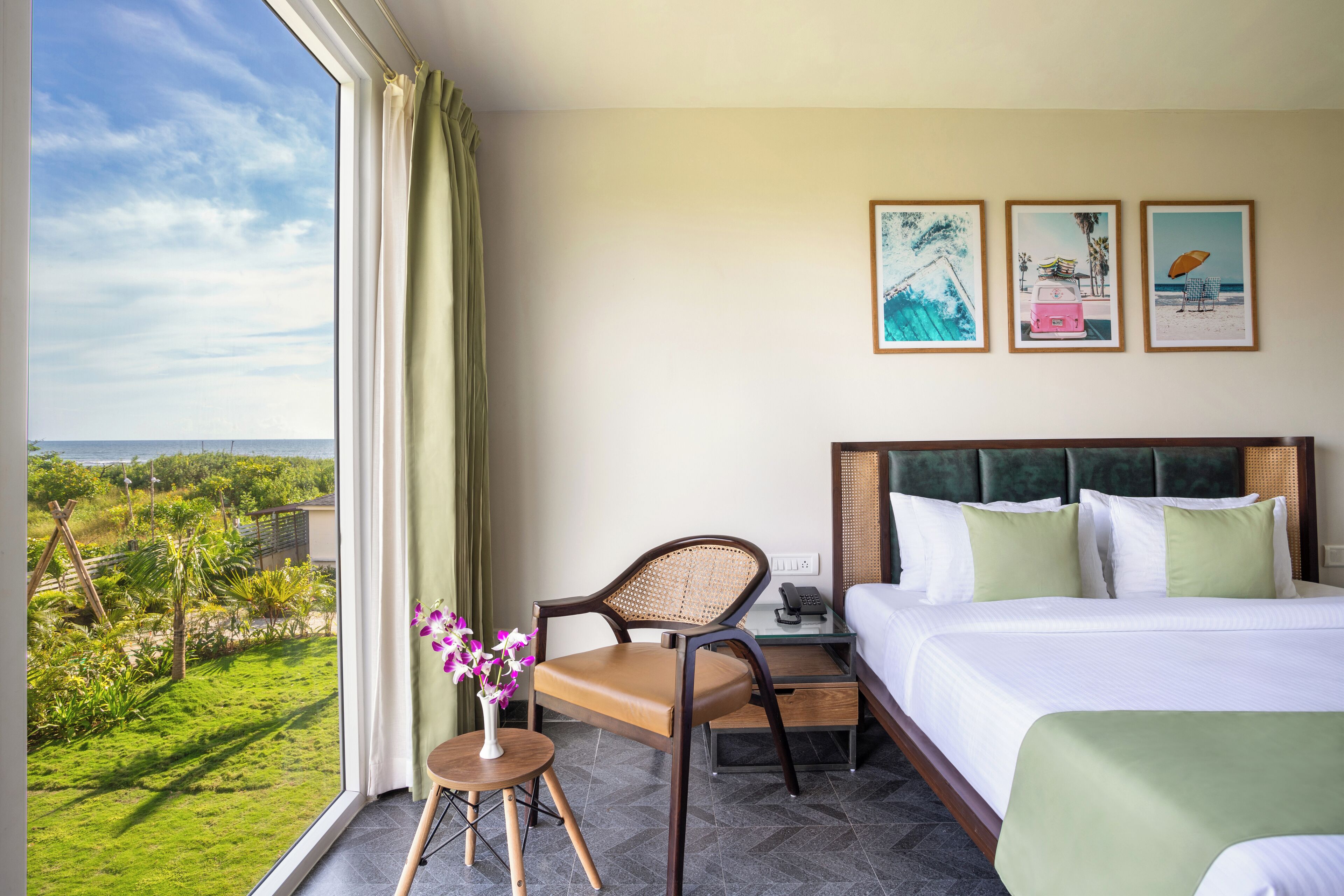 A hotel room with a bed, a chair, a small table with a vase, and a view of the outdoors.