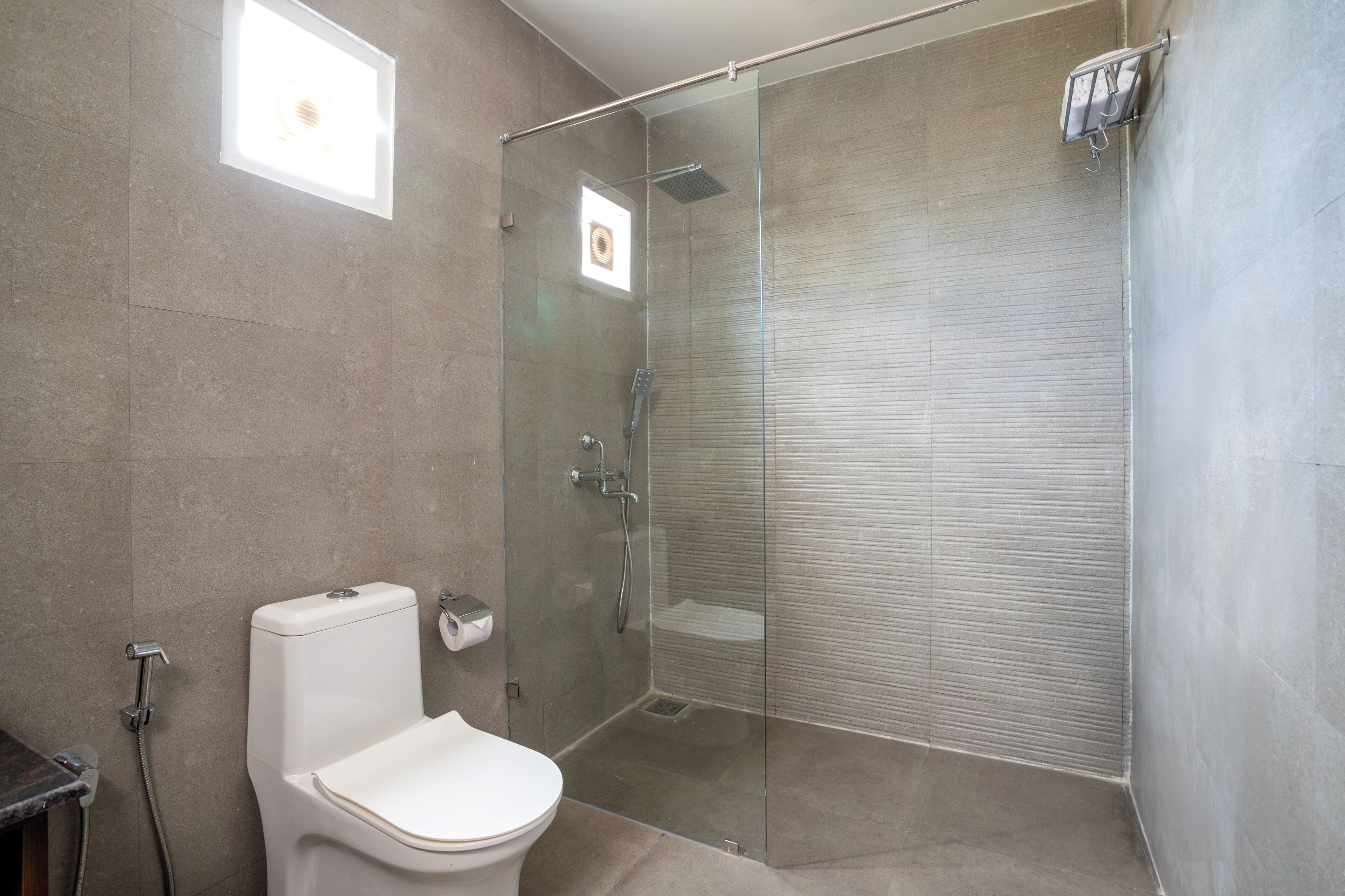 A modern bathroom with a glass-enclosed shower, a toilet, and a small window.