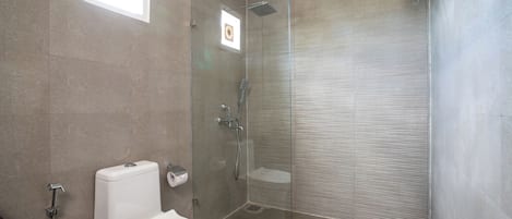 A modern bathroom with a glass-enclosed shower, a toilet, and a small window.