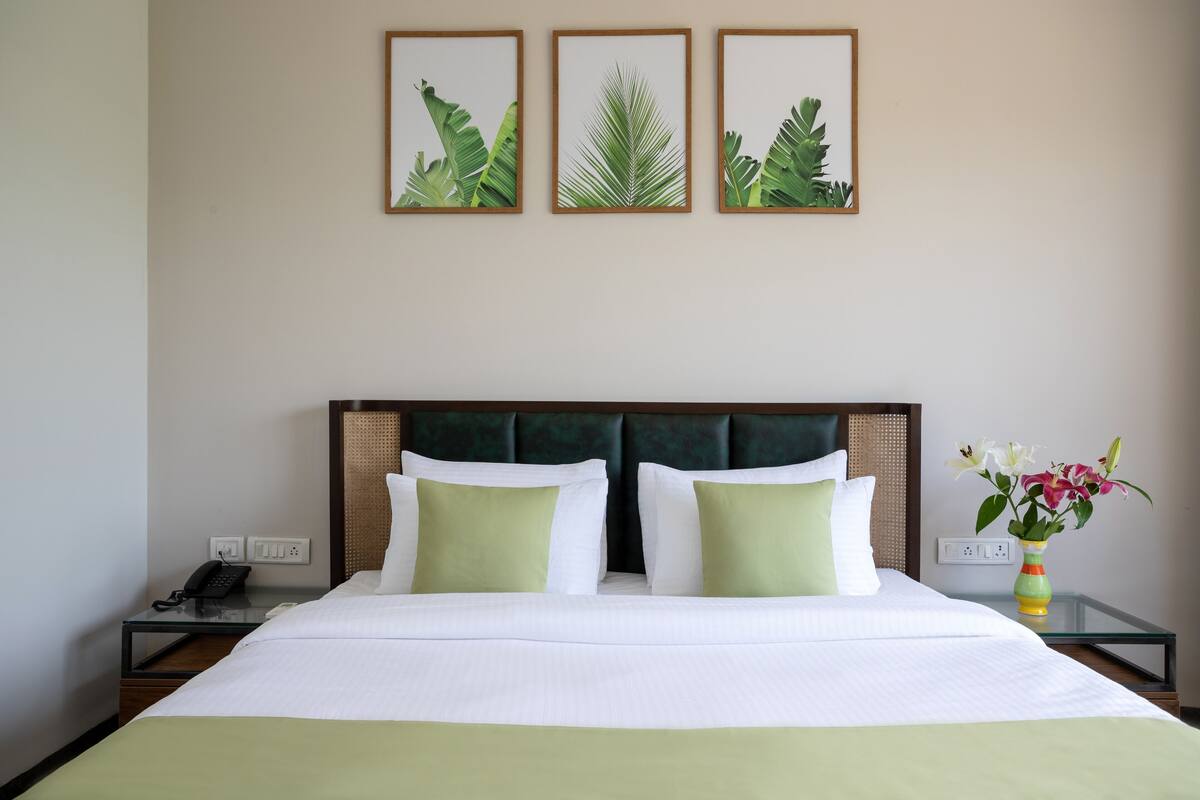 Una habitación de hotel con una cama, dos mesitas de noche, un teléfono y un florero con flores.
