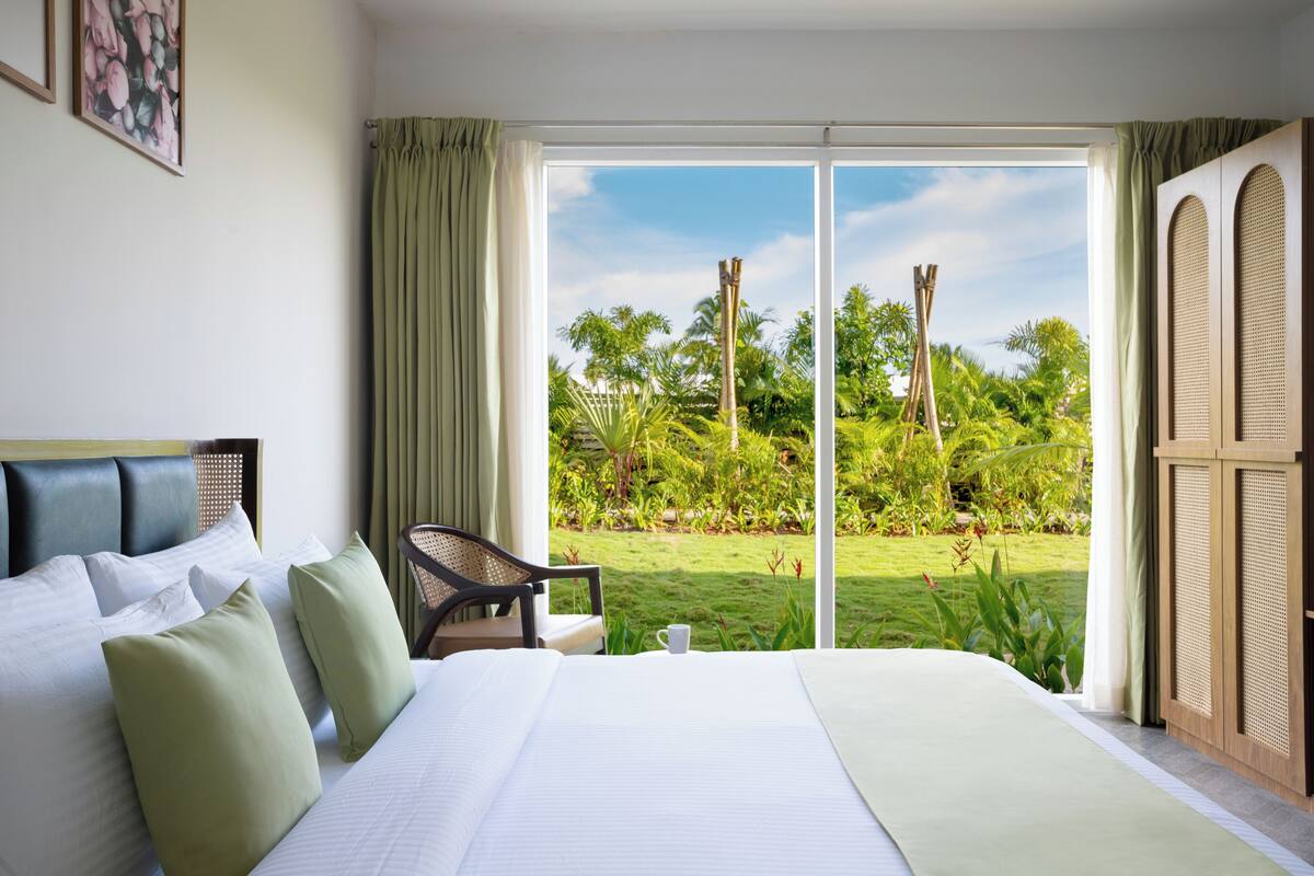 Habitación de hotel con una cama grande, una silla y vista a un jardín a través de una puerta corrediza.