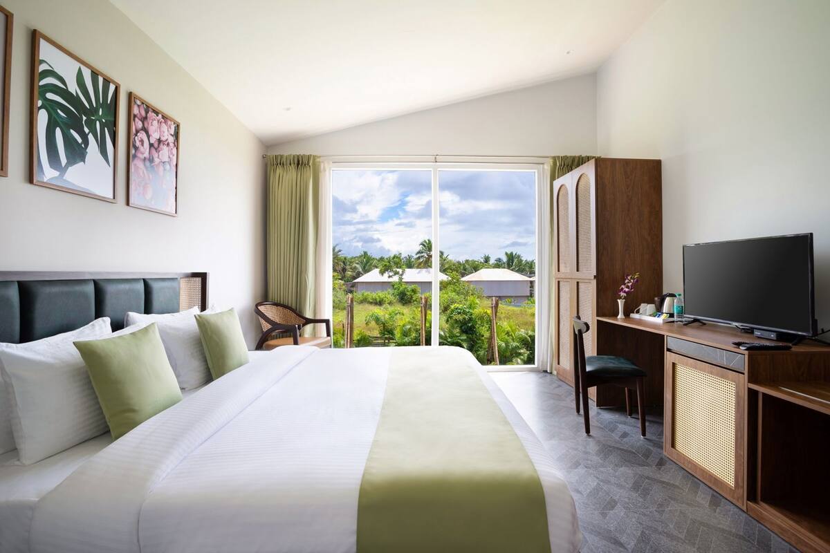 Habitación de hotel con una cama grande, un escritorio con televisor y vistas a zonas verdes.