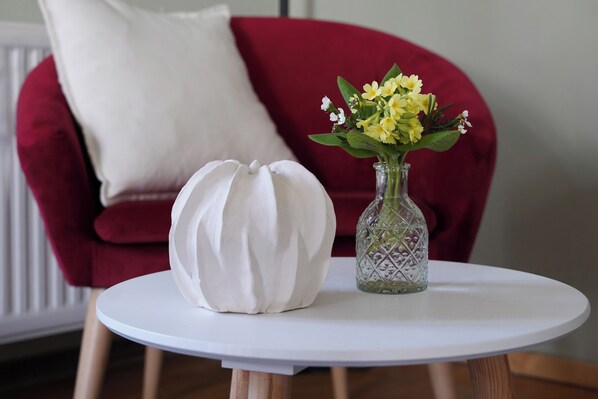 A white round table with a white cushion and a clear glass vase with yellow flowers.