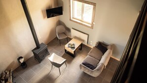 A cozy living room with a fireplace, a sofa, a coffee table, and a TV mounted on the wall. - LA TRANQUILITE NORMANDE Country cottage surrounded by animals! (Livarot-Pays-d'Auge)