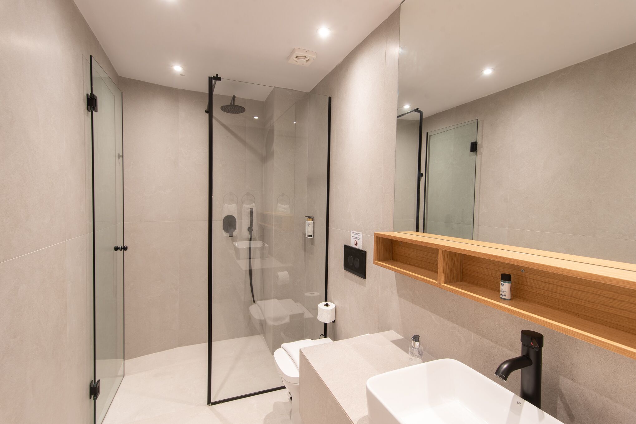 Un baño moderno con ducha de vidrio, inodoro, lavamanos y espejo.