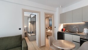A modern kitchen with a built-in oven, a coffee maker, and a sink. There is a dining area with a table and chairs. - The Residences Kalamata (Kalamata)