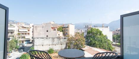 A balcony with two chairs and a small table, overlooking a cityscape with buildings and a clear sky.