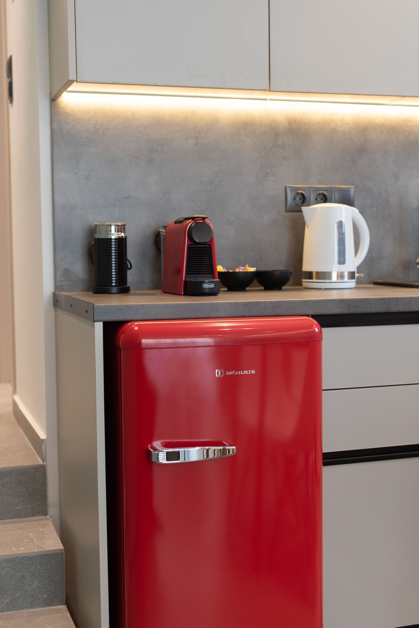 A compact kitchen with a red refrigerator, a coffee maker, and a kettle on the countertop.