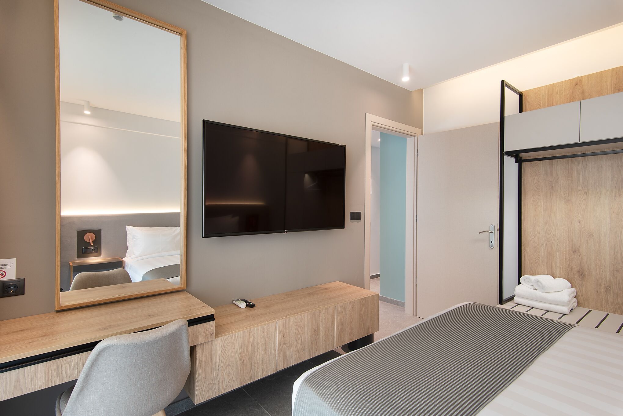 Una habitación de hotel moderna con una cama grande, un escritorio con una silla, un televisor de pantalla plana en la pared y un armario con espejo.