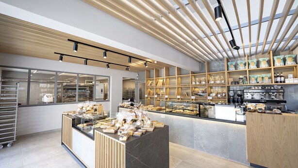 A bakery with a modern design, featuring wooden shelves, a display counter with baked goods, and a coffee machine. - The Residences Kalamata (Kalamata)