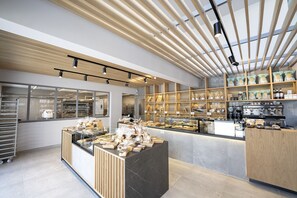 A bakery with a modern design, featuring wooden shelves, a display counter with baked goods, and a coffee machine. - The Residences Kalamata (Kalamata)