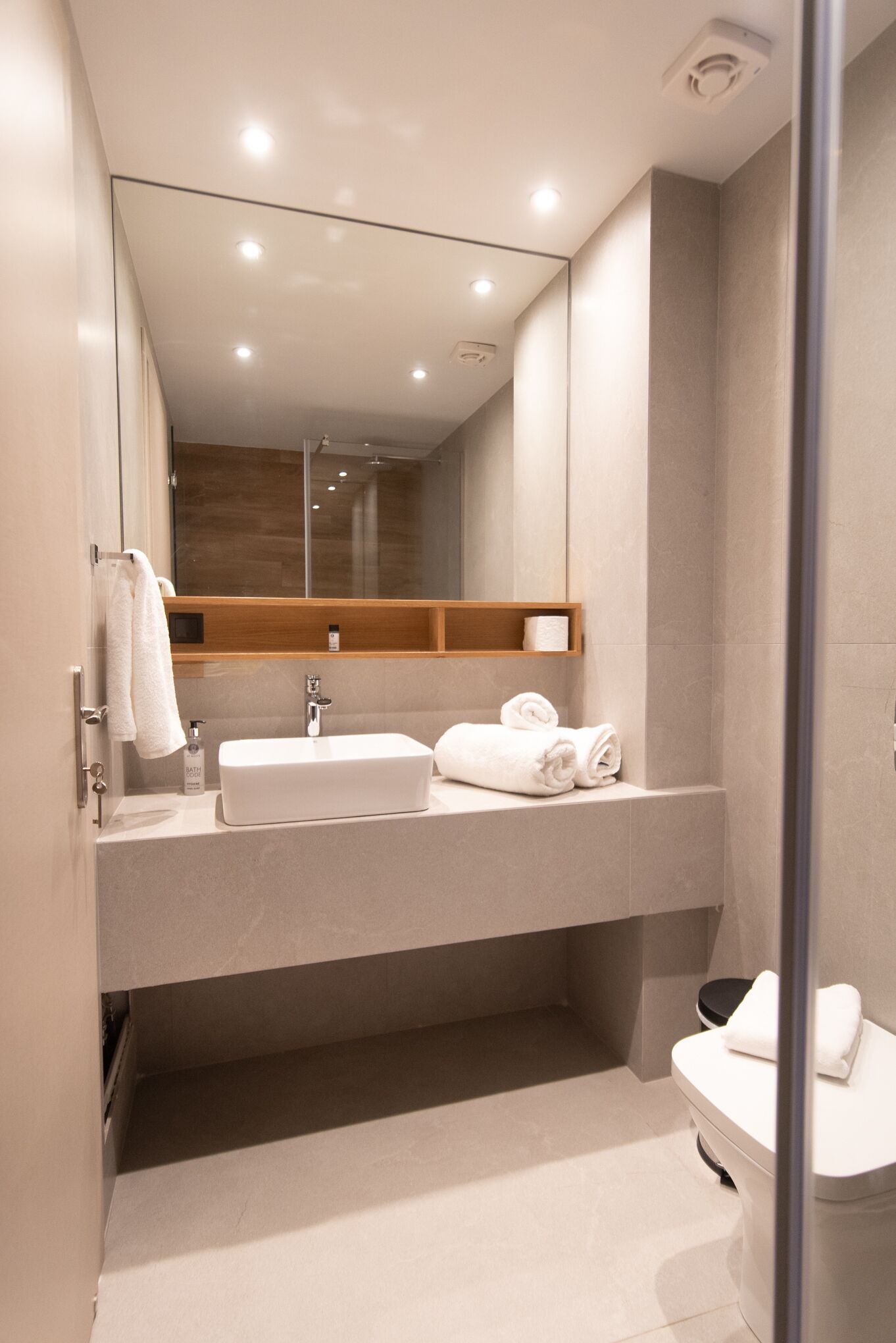 A modern bathroom with a large mirror, two sinks, a toilet, and a shower area.
