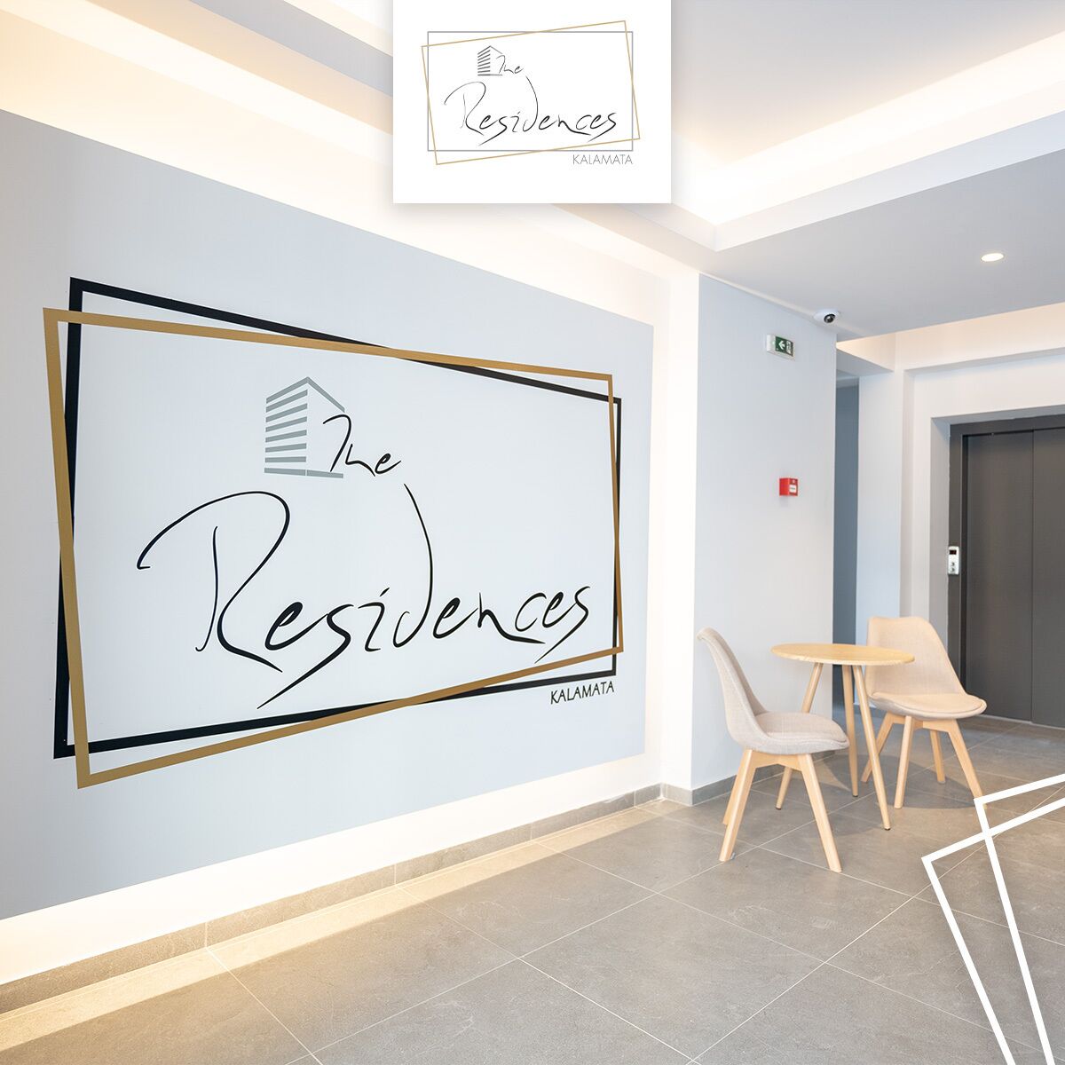 Un moderno vestíbulo de hotel con un cartel enmarcado grande que dice "The Residences Kalamata" y un área de descanso con dos sillones y una pequeña mesa.