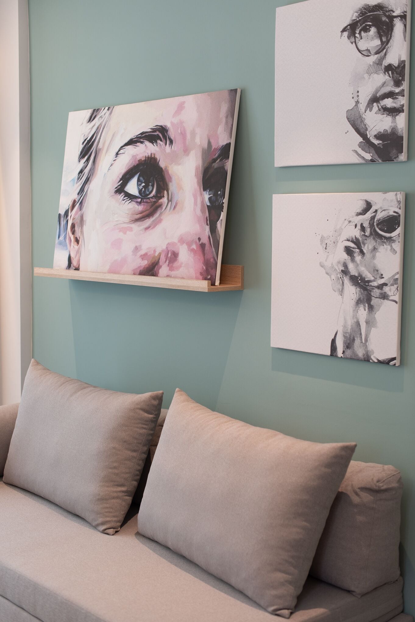 Ein Zimmer mit einer hellblauen Wand, einem beigen Sofa mit zwei Kissen und drei Bildern an der Wand.