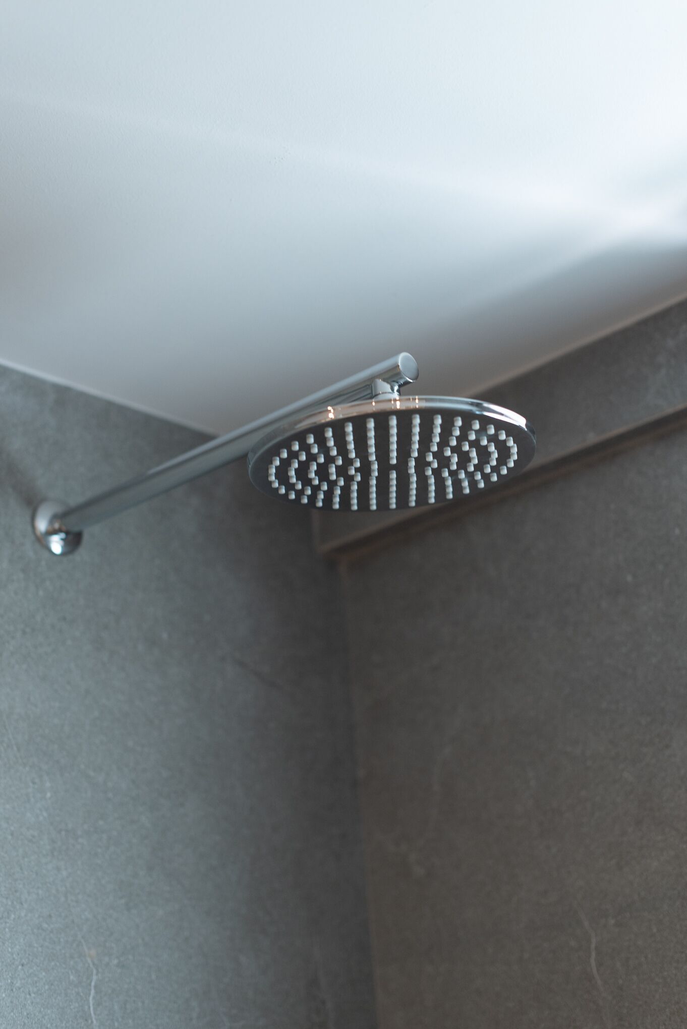 Un cabezal de ducha con diseño curvo, instalado en una pared de baño con superficie texturizada.
