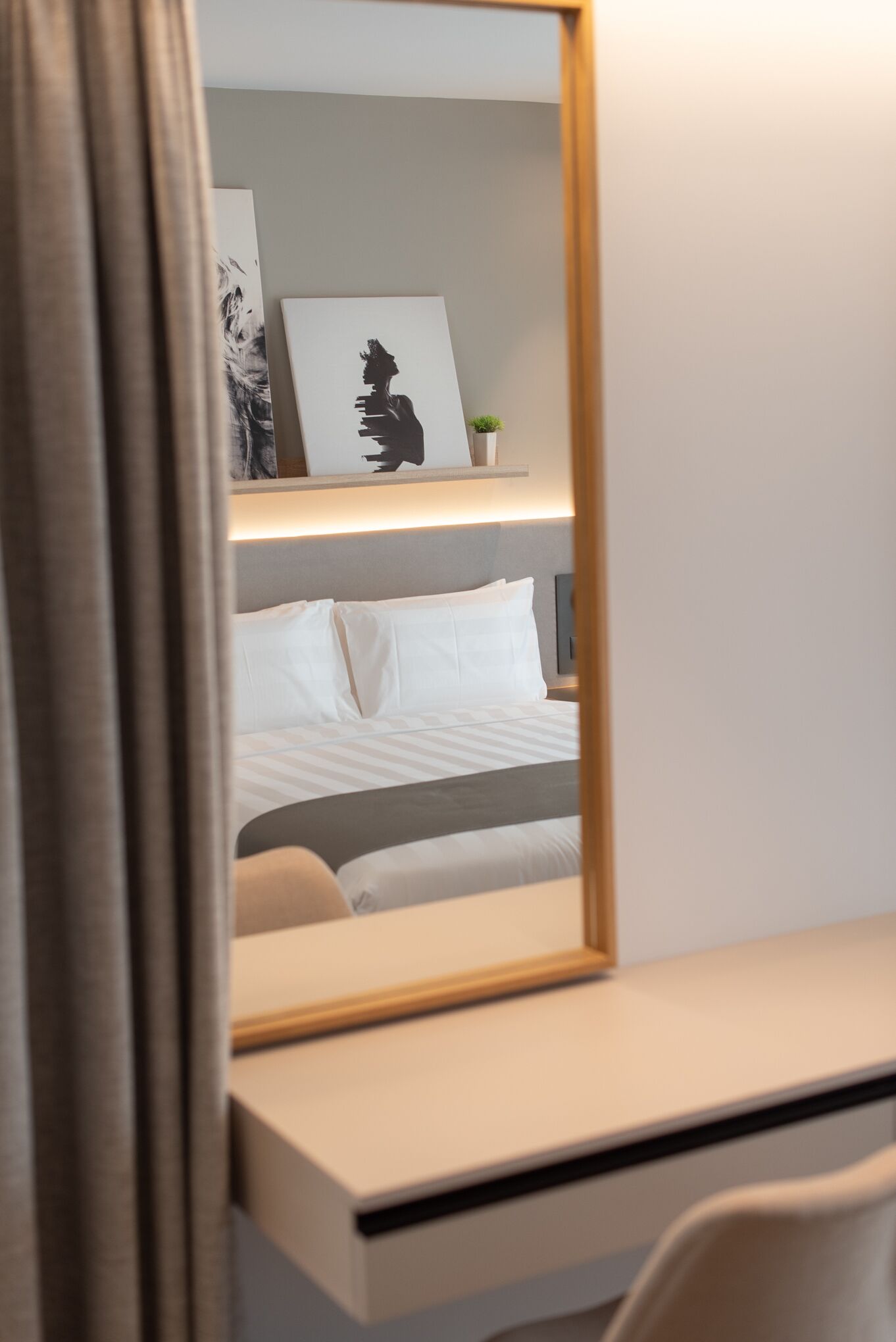 A hotel room with a bed, a desk, and a mirror reflecting the room.