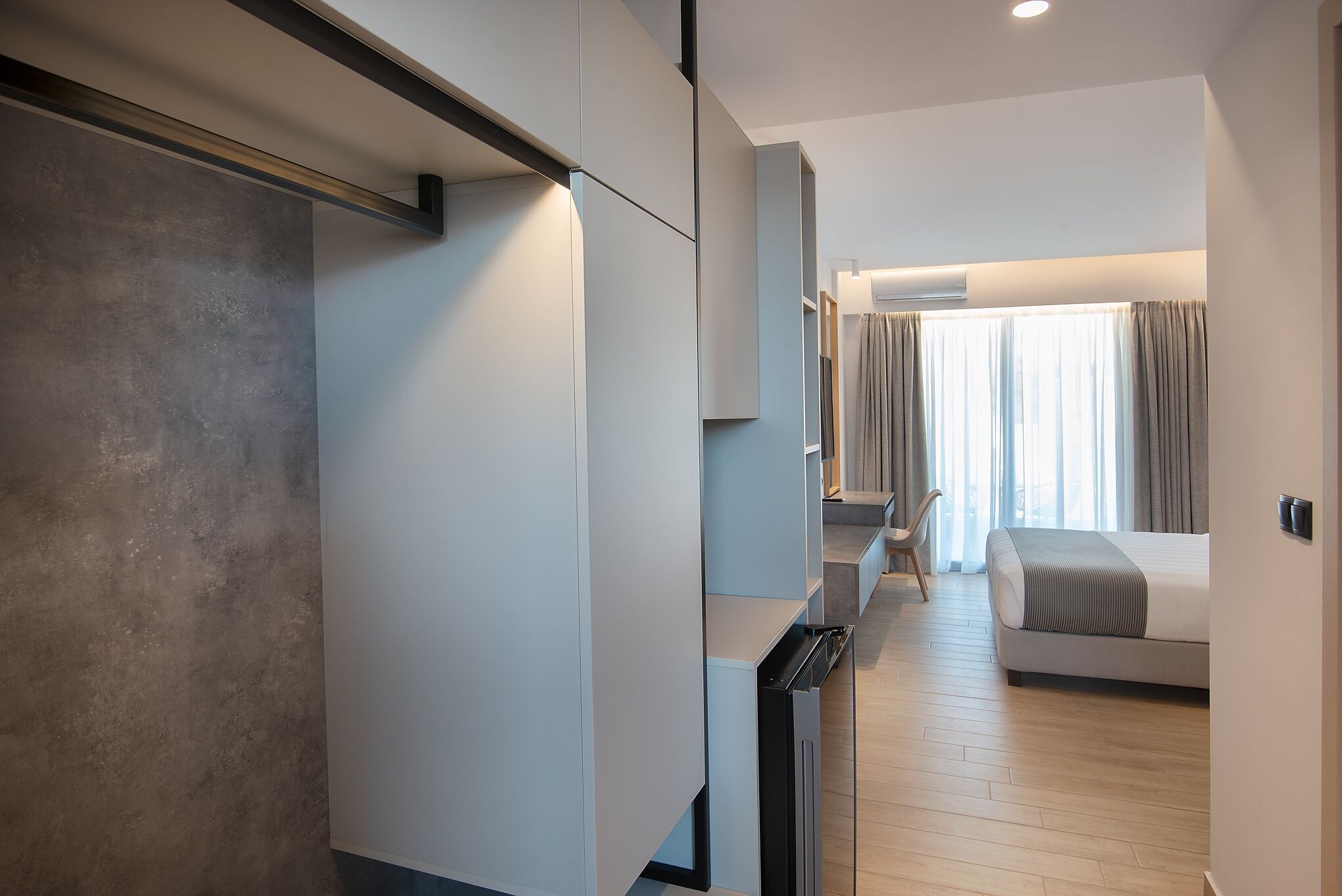 Habitación de hotel moderna con diseño minimalista, que incluye una cama grande, un escritorio integrado y vistas de la ciudad a través de amplias ventanas.