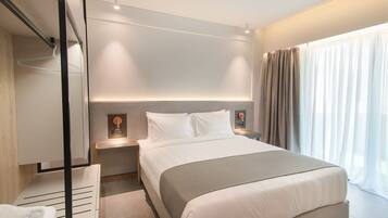 A modern hotel room with a large bed, bedside tables, a hanging light, and a view of the outdoors through sheer curtains.