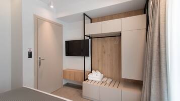 A modern hotel room with a bed, a TV mounted on the wall, a wooden bench, and a storage unit with towels.