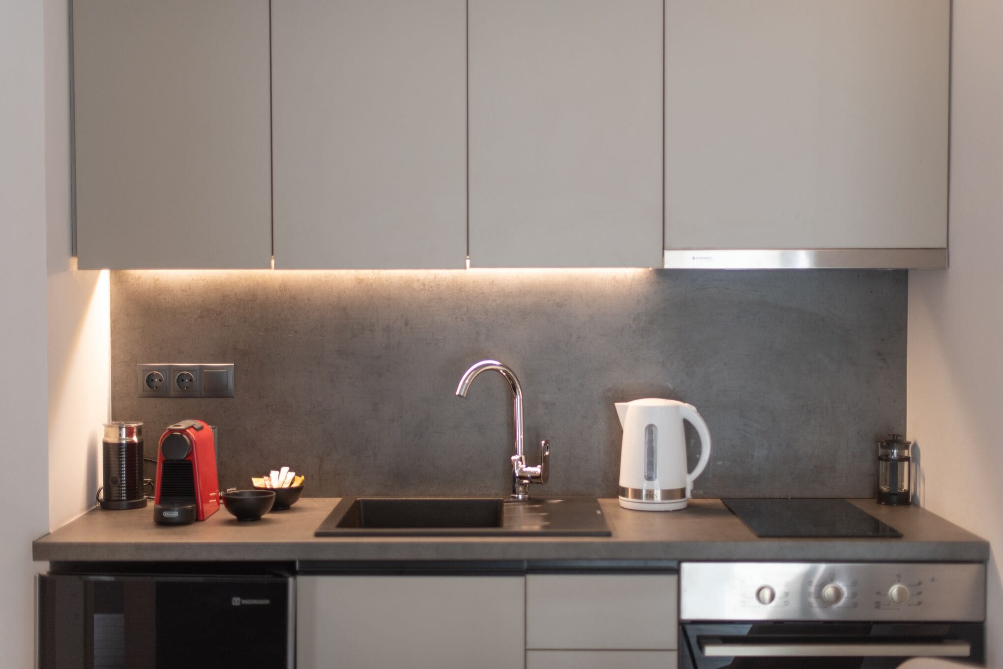 Una cocina moderna con un lavamanos de acero inoxidable, una tetera y una cafetera.