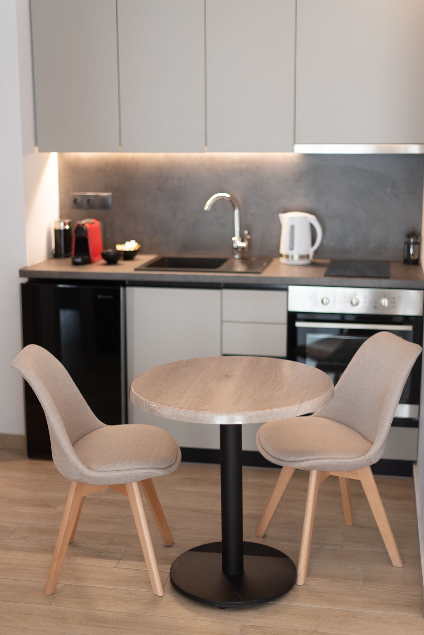 A modern kitchen with a round table and two chairs, a dishwasher, a coffee maker, and an oven.