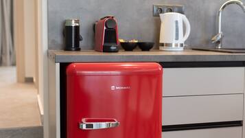 Una cucina compatta con un elettrodomestico rosso, una macchina da caffè e un bollitore sul piano di lavoro.