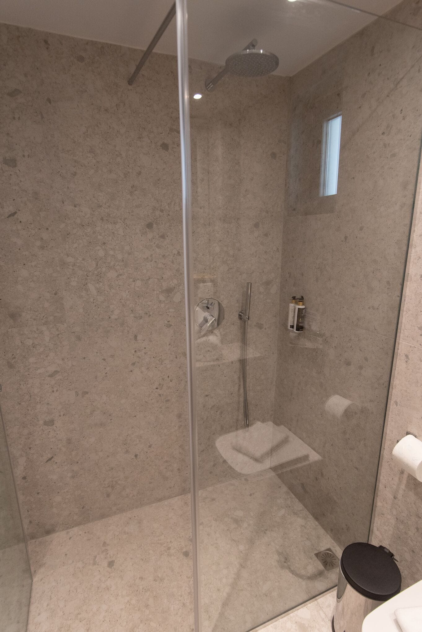 A modern bathroom with a glass-enclosed shower, a small window, and a toilet.