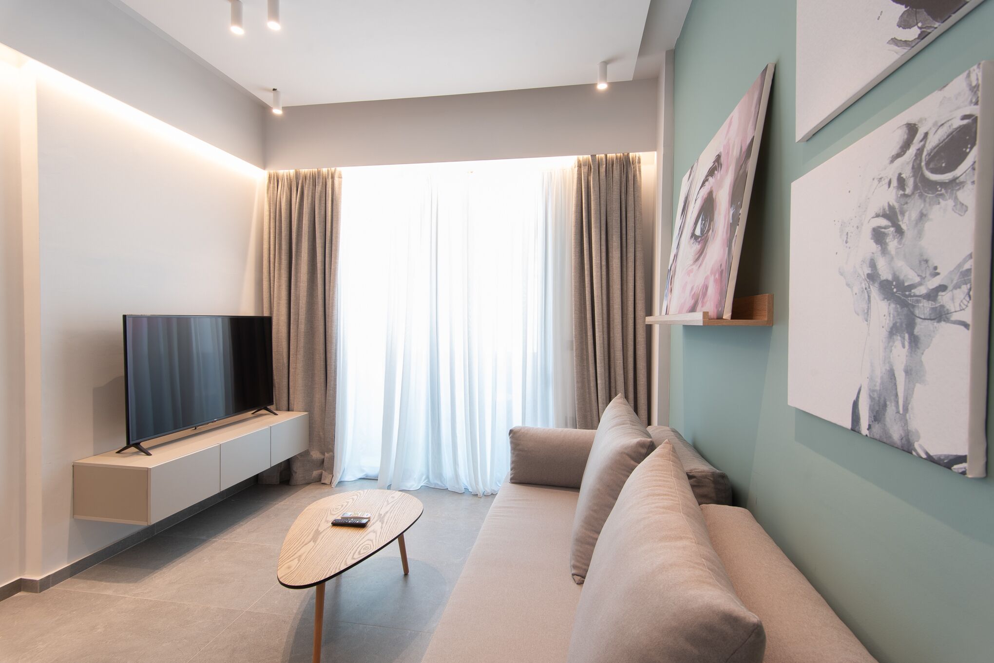 Un salon moderne avec un téléviseur à écran plat posé sur une étagère intégrée, un canapé beige, une petite table basse en bois et des œuvres d’art accrochées aux murs.
