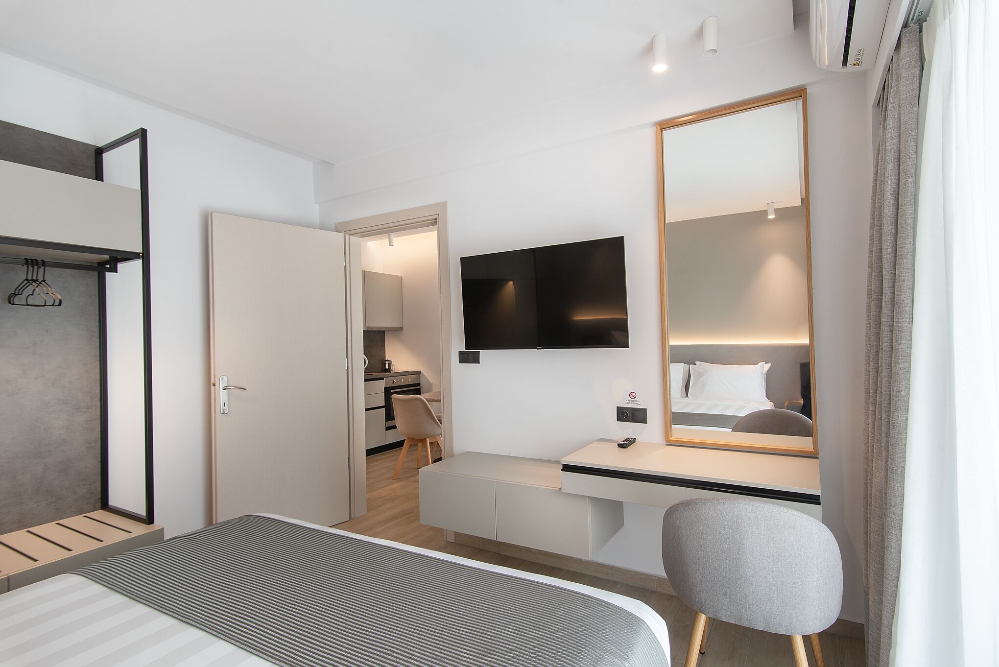 A modern hotel room with a bed, a desk, a chair, a large mirror, and a TV.