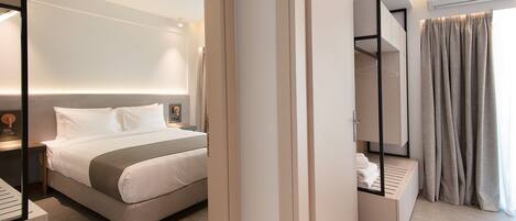 A modern hotel room with a neatly made bed, built-in wardrobe, and a large window with curtains.