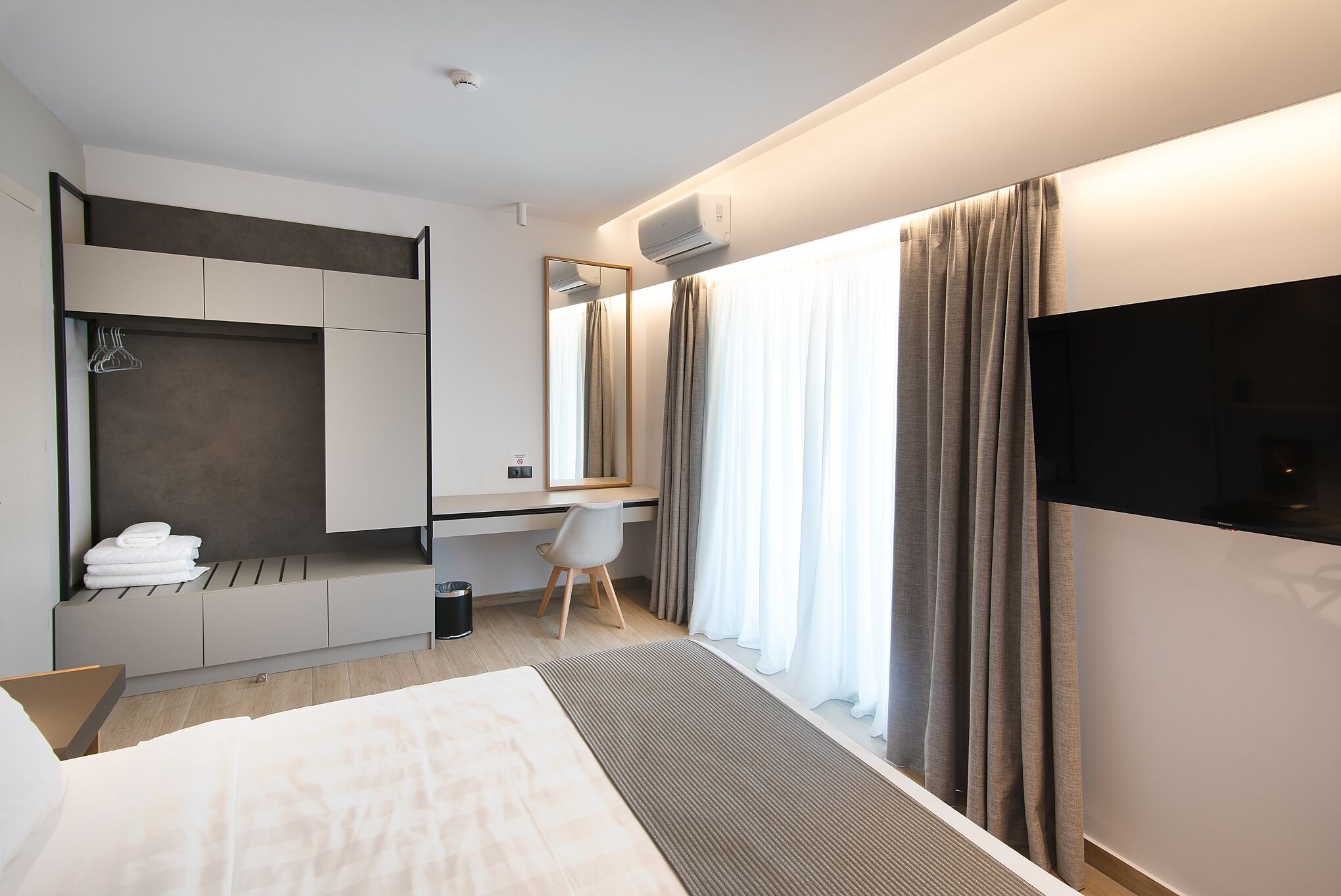 Une chambre d’hôtel moderne équipée d’un lit, d’un bureau, d’une chaise, d’une télévision et d’une grande fenêtre avec des rideaux.