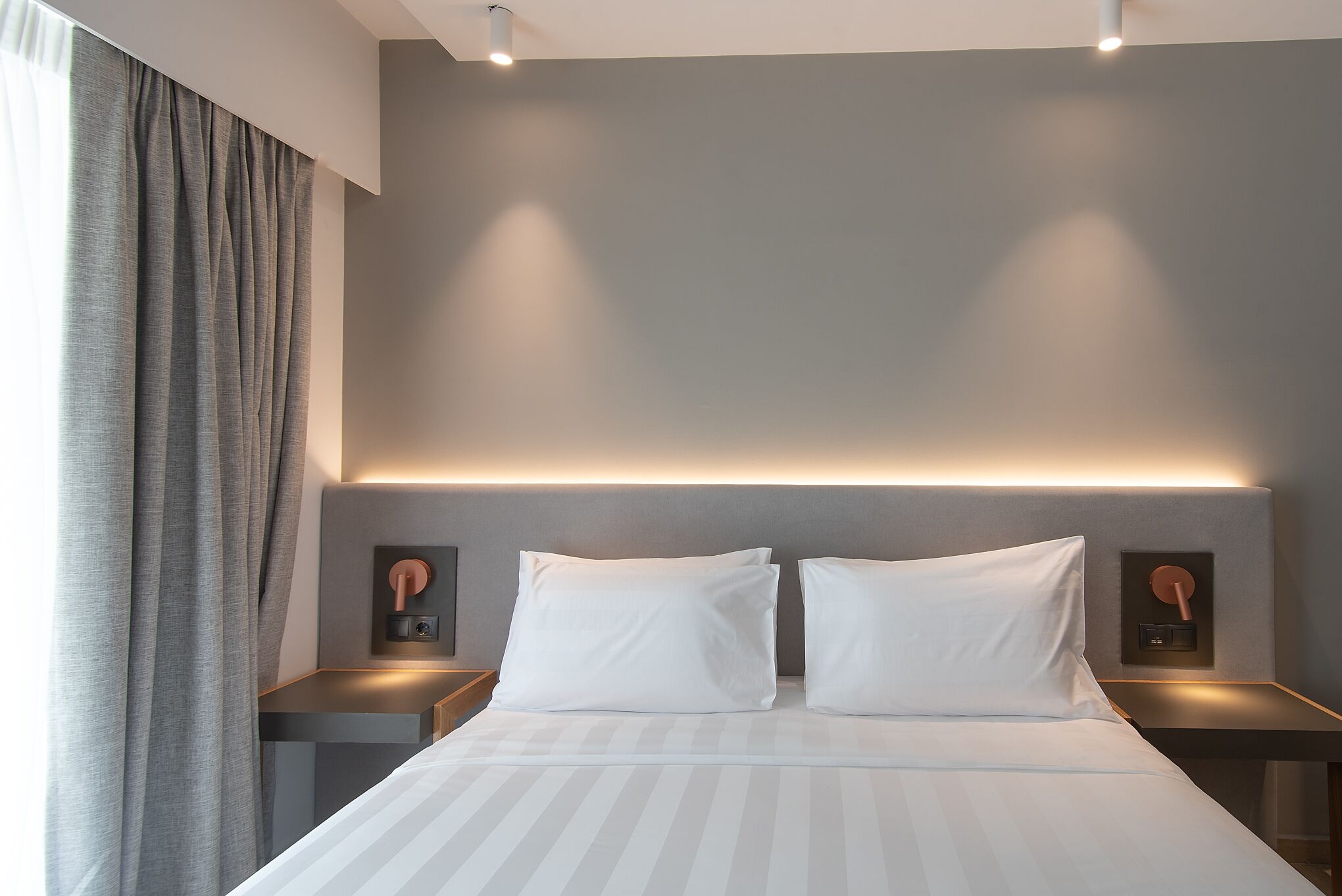 A modern hotel room with a large bed, two bedside tables, and a wall-mounted light fixture.