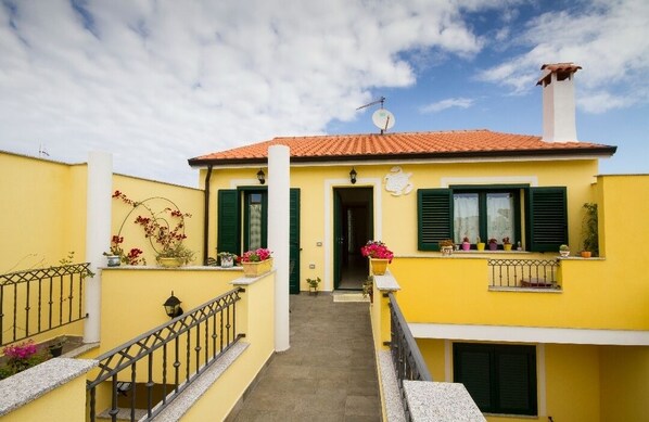 Un bâtiment jaune avec des volets verts, un toit en tuiles et une antenne parabolique.