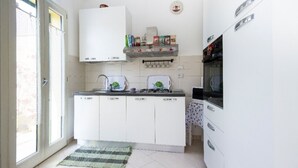 A kitchen with white cabinets, a gas stove, a microwave, and a small shelf with jars. - apartment with terrace (Sant'Antioco)