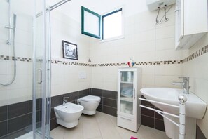 Une salle de bain moderne dotée d’une douche à parois de verre, d’un bidet, de toilettes, d’un lavabo et d’un meuble avec des portes en verre.