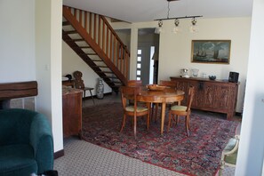 Un coin repas avec une table et des chaises en bois, un escalier et un tableau accroché au mur.