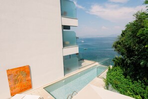 Un hotel moderno con piscina infinita de vidrio con vistas al mar, cielo despejado y un letrero que dice Pay Hotel Beach & Restaurant.