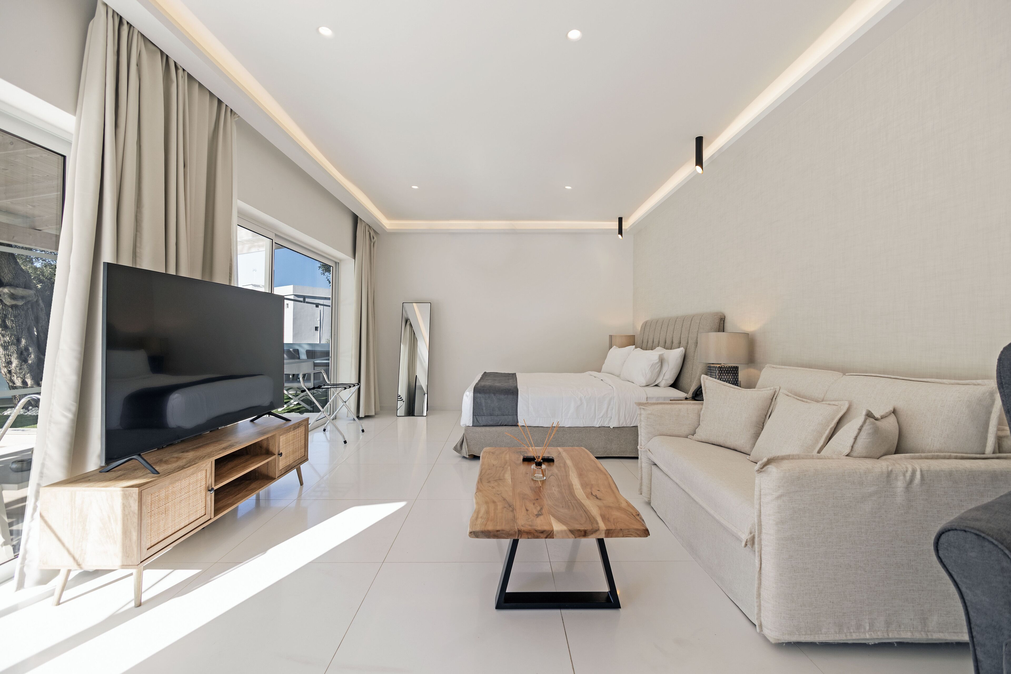 A modern living room with a flat-screen TV, a wooden coffee table, a sofa, and a bed.
