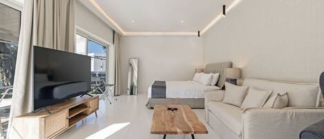 A modern living room with a flat-screen TV, a wooden coffee table, a sofa, and a bed.