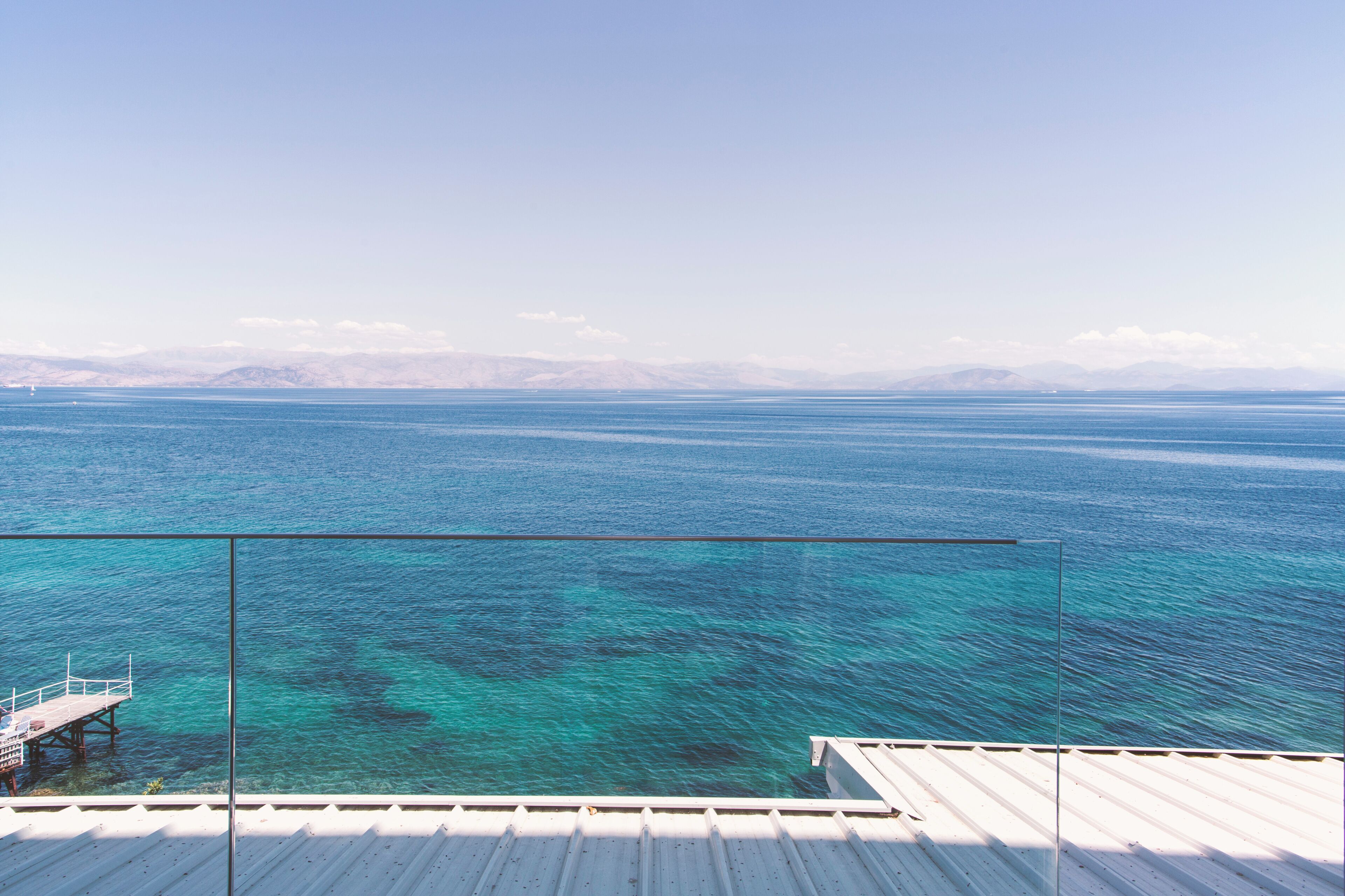 A clear view of the ocean from a balcony with a wooden deck and glass railing.