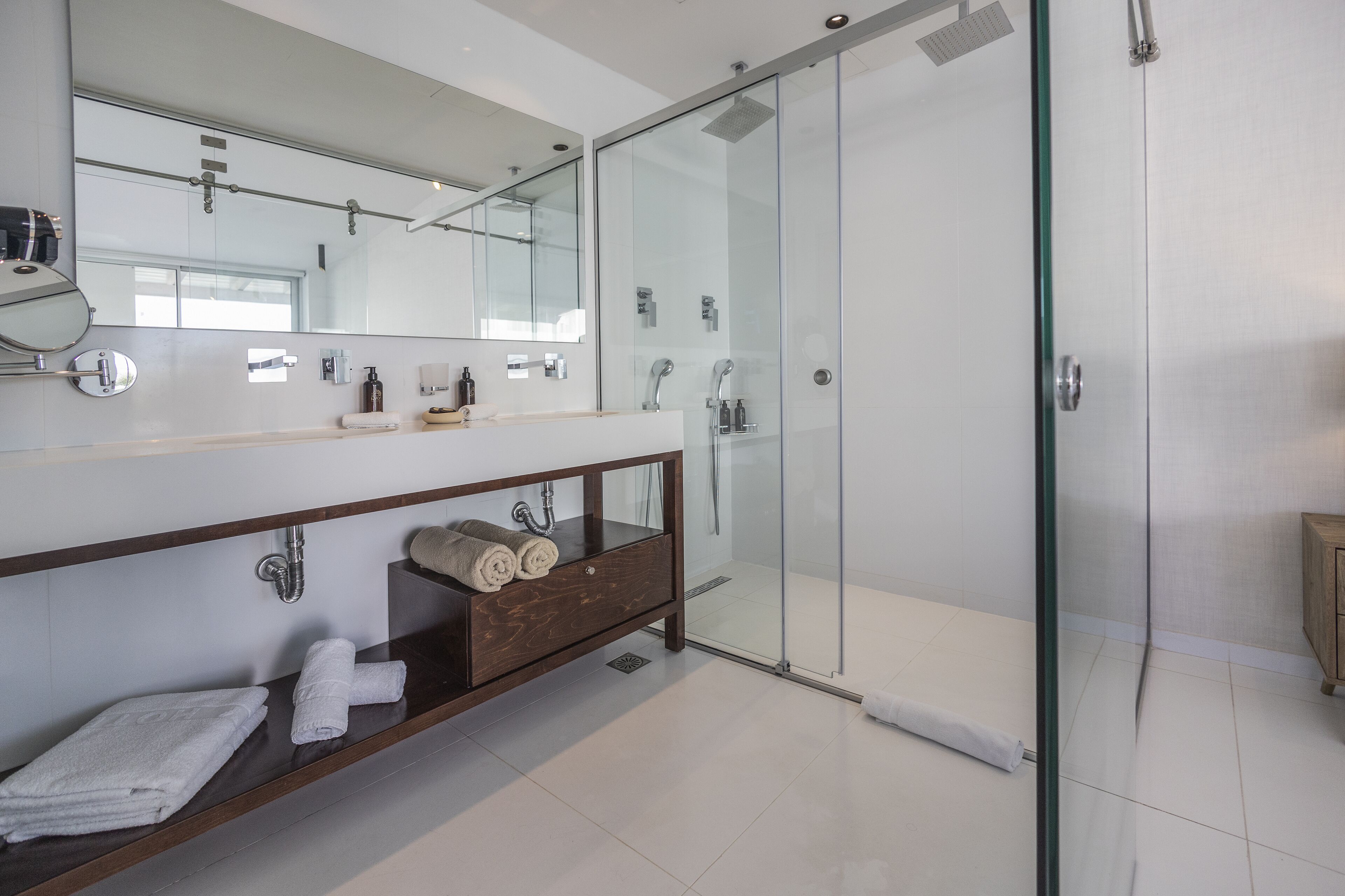 Un baño moderno con ducha de vidrio, tocador de madera con espejo y toallas dobladas con cuidado.
