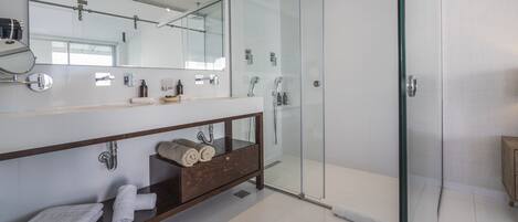 Un baño moderno con ducha de vidrio, tocador de madera con espejo y toallas dobladas con cuidado.