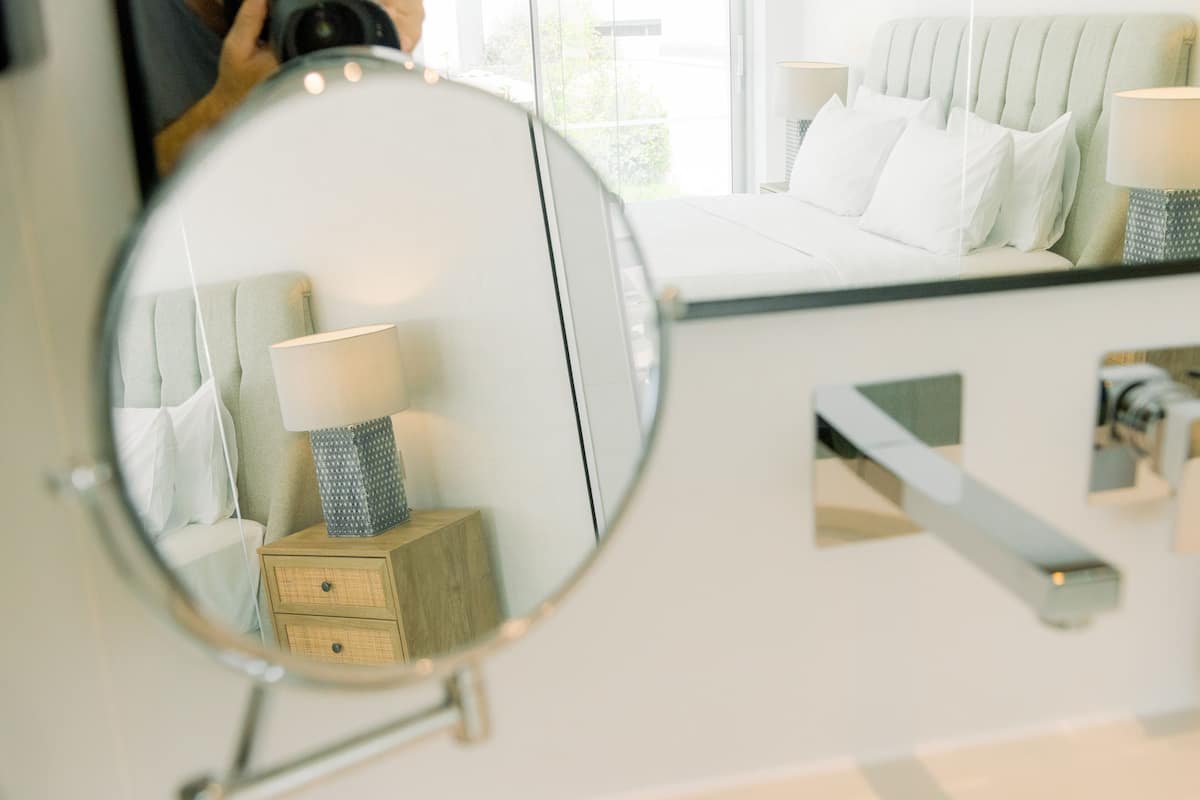 Un dormitorio con cama, lámparas de noche y un espejo que refleja la habitación.