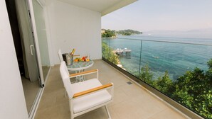 A balcony with a table and chairs, overlooking a coastal view with a clear sky. -  Ray Hotel Corfu (Corfu)