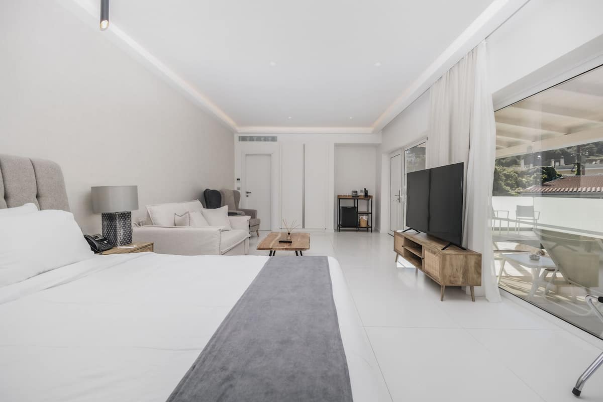 Una habitación de hotel moderna con una cama grande, un sofá, un televisor y un balcón con puerta de cristal.