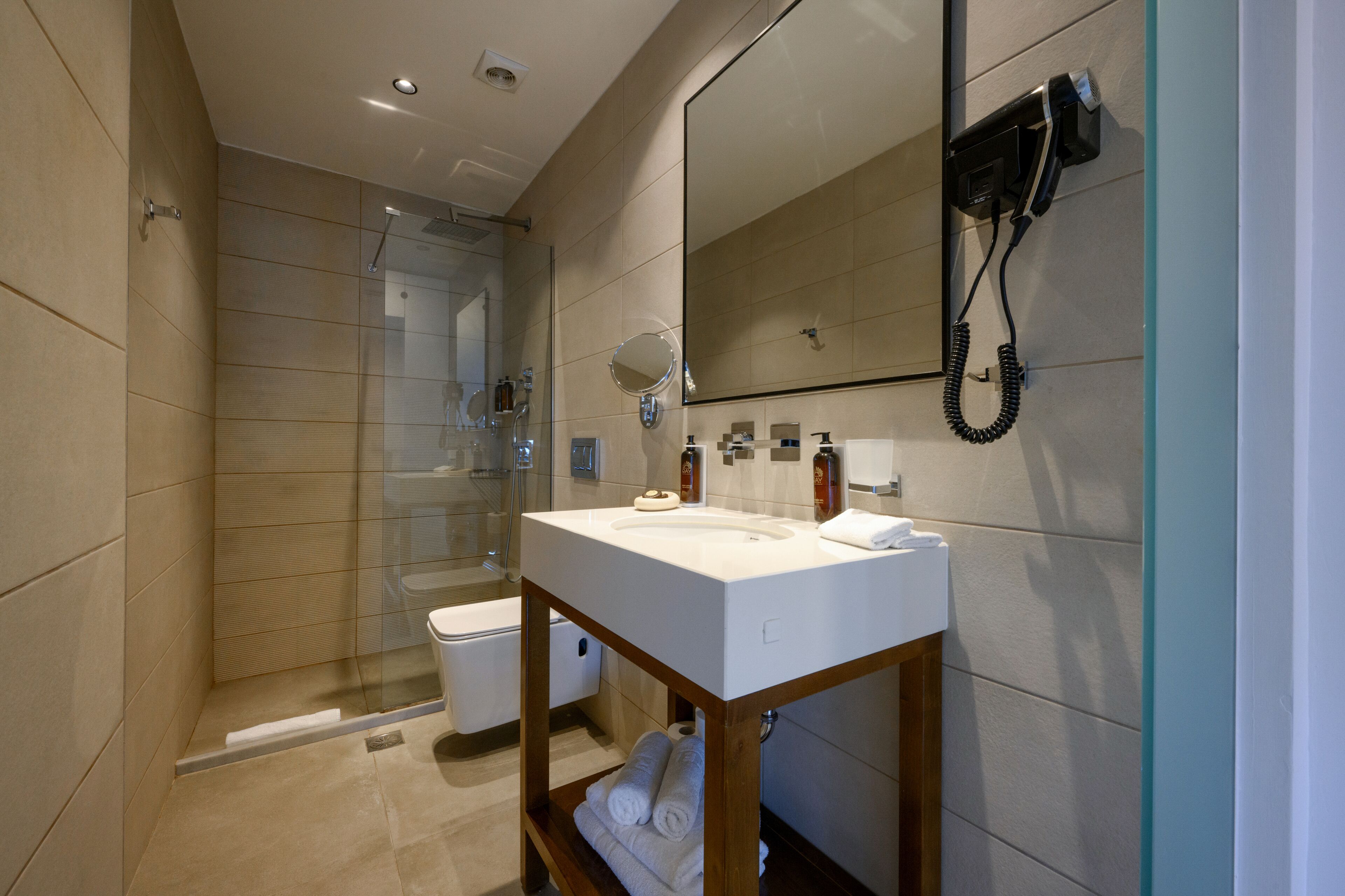 Un baño moderno con cabina de ducha de vidrio, un lavamanos blanco con espejo y un secador de pelo montado en la pared.