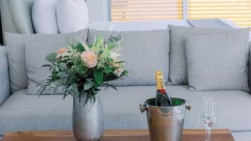 A living room with a grey sofa, a metal bucket with a bottle of champagne, and a vase with flowers on a wooden table.